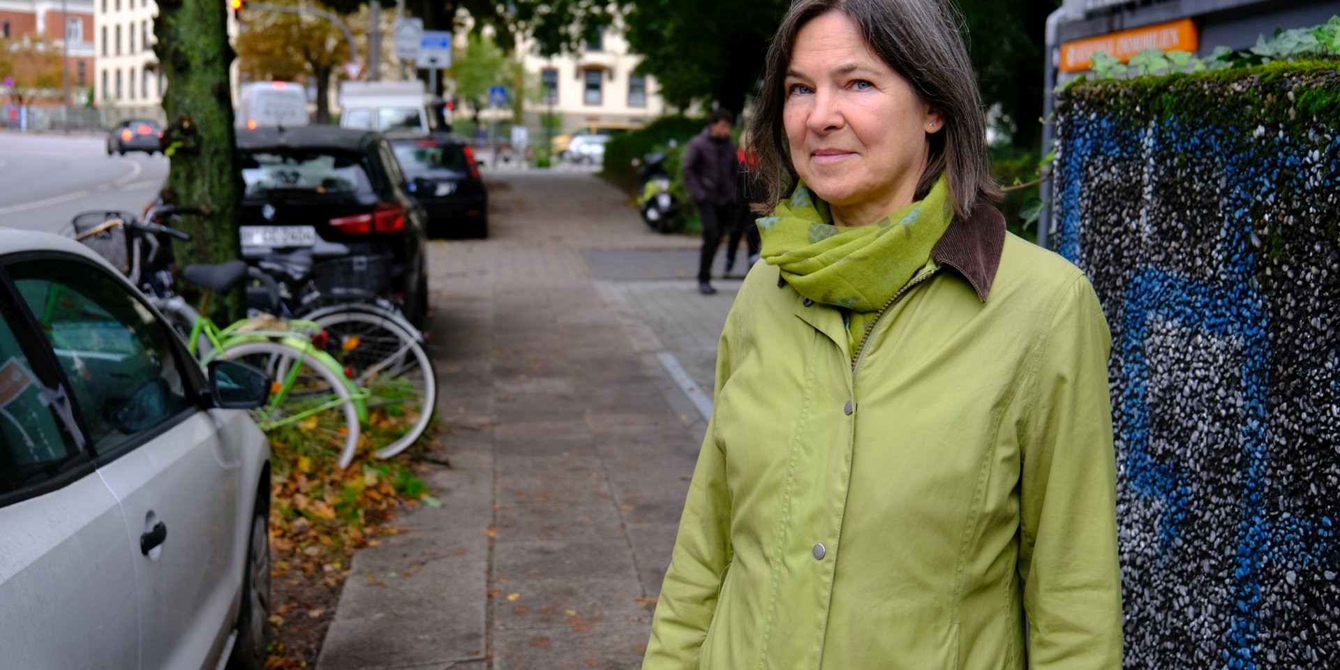 Simone Dietz an einer der vielen schmalen Gehwegstellen. Hier müssen sich Fußgänger*innen heute noch zwischen parkenden Autos und Müllcontainerboxen hindurchzwängen