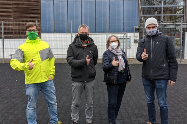 vlnr: Timo B. Kranz (GRÜNE), Michael Stuhr (Stellv. Vorsitzender SiB-Club), Maren Schindeler-Grove (1. Vorsitzende SiB-Club), Carsten Heinrich (Stellv. Schulleiter der Stadtteilschule Am Heidberg) auf der Fläche, die überdacht werden soll. Auf dem Schulgelände herrscht strenge Maskenpflicht