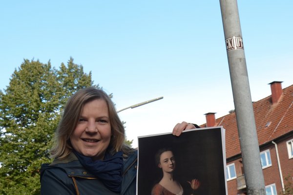 Simone Dornia an der Dennerstraße mit einem Gemälde von Catharina Denner, das ihr Vater Balthasar malte. Allein nach ihm ist die Straße bisher benannt