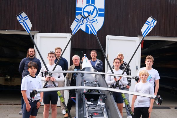 Oliver Camp (GRÜNE, rechts hinter dem Boot) und Nicklas Homuth (RVW, letzte Reihe, 2. von links) mit Trainern und Sportler*innen des Vereins