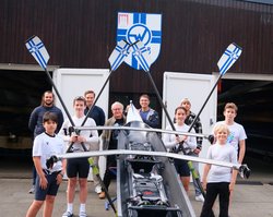 Oliver Camp (GRÜNE, rechts hinter dem Boot) und Nicklas Homuth (RVW, letzte Reihe, 2. von links) mit Trainern und Sportler*innen des Vereins