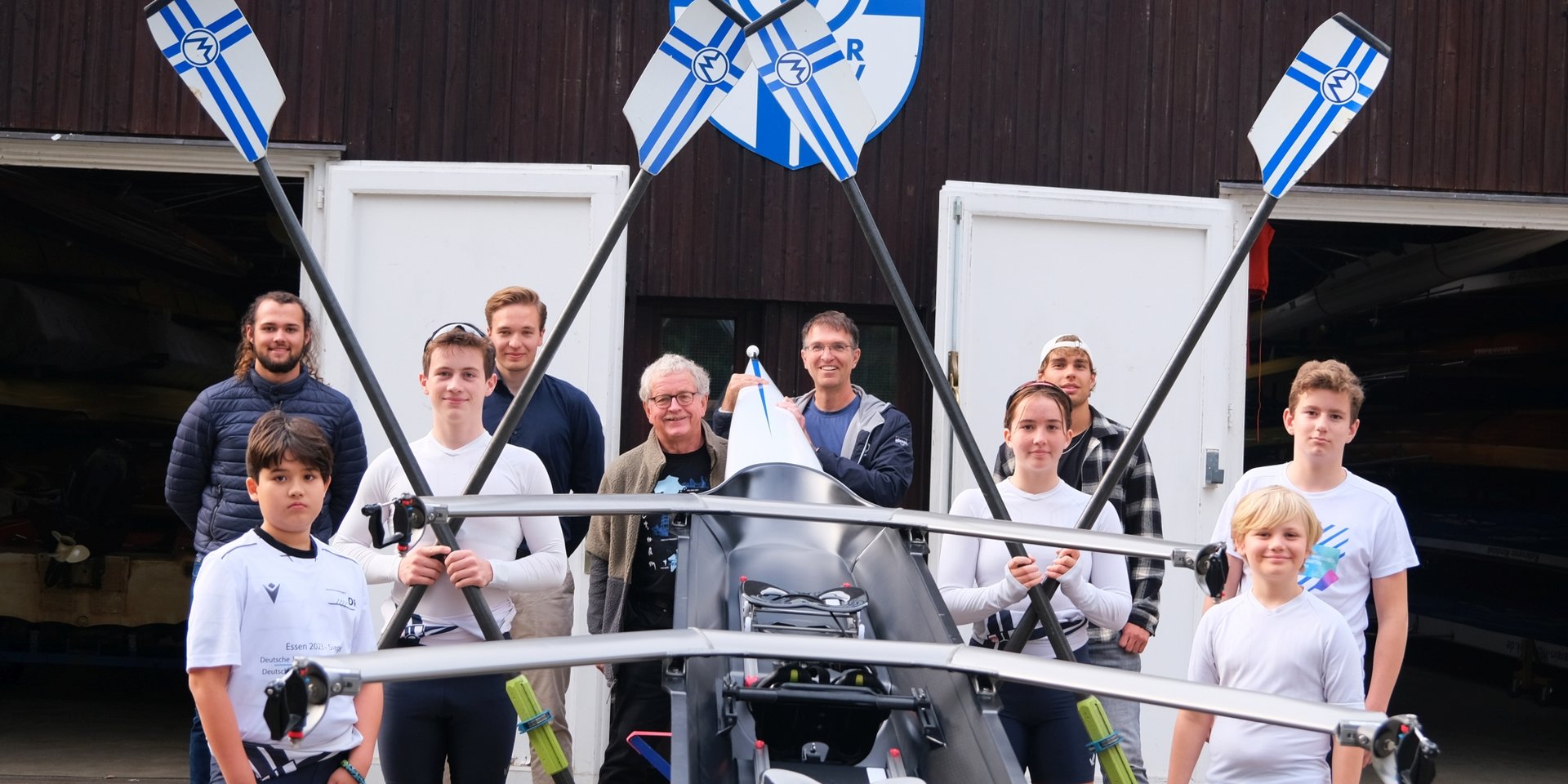 Oliver Camp (GRÜNE, rechts hinter dem Boot) und Nicklas Homuth (RVW, letzte Reihe, 2. von links) mit Trainern und Sportler*innen des Vereins